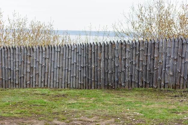 Фото Ветхий забор в солнечный весенний день. фоновая текстура старого серого деревянного забора из целых бревен с узлами. натуральный материал.