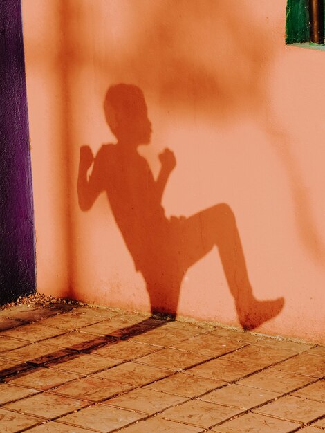 A shadow of a boy playing with the light against orange wall