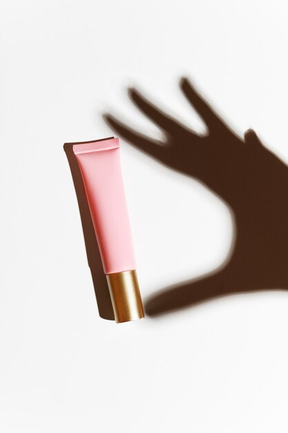 Shadow of a hand with a pink tube of cream