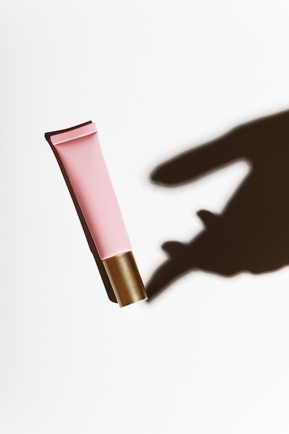 Shadow of a hand with a pink tube of cream