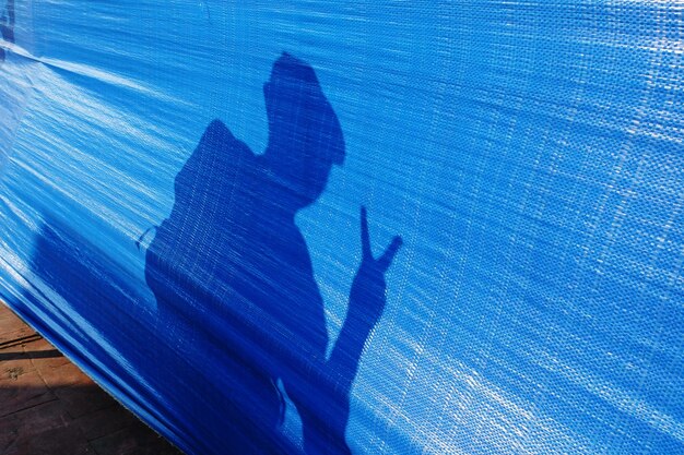 Shadow of man showing peace sign on blue tarpaulin