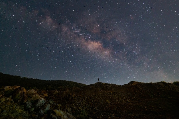 山の上に立つ男の影は、美しい天の川の星の背景を持っています。