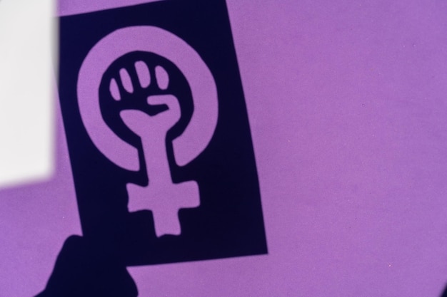 Photo shadow of the symbol of the fight for feminism on a purple background, clenched fist of a woman in the march protests for women's rights and for equality