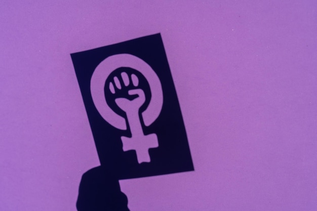 Photo shadow of the symbol of the fight for feminism on a purple background, clenched fist of a woman in the march protests for women's rights