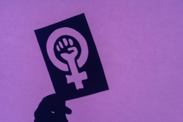 紫色の背景にフェミニズムの戦いの象徴の影、行進中の女性のくいしばられた握りこぶしが女性の権利に抗議