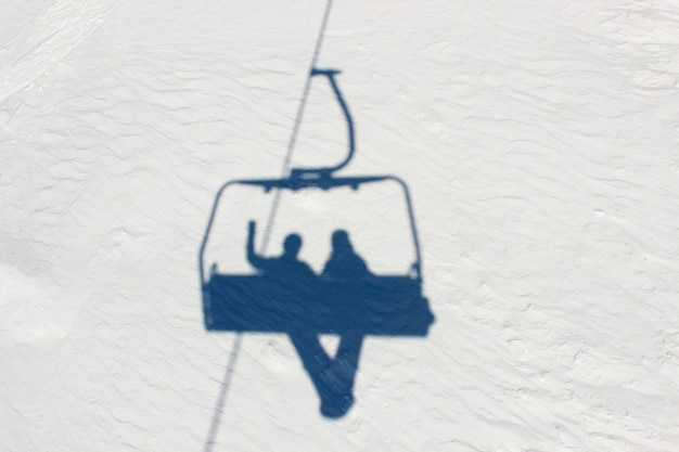Тени на снегу двух сноубордистов, поднимающихся в гору на подъемнике