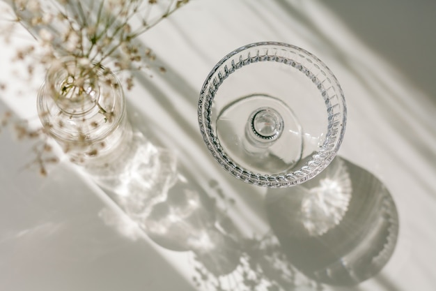 Shadows on a white background from a glass and flowers. Dried flowers in a glass vase in the rays of light. Home.