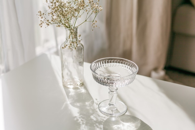 Shadows on a white background from a glass and flowers. Dried flowers in a glass vase in the rays of light. Home.