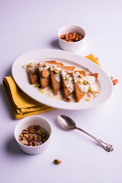 Shahi tukda 또는 Double ka metha는 연유, 견과류 및 Mawa/khoya로 장식된 버터 버터의 빵 푸딩입니다. 인기 있는 인도 디저트, 변덕스러운 배경 위에 접시에 제공됩니다. 선택적 초점