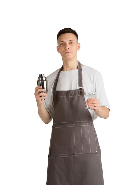 Shaker. Portrait of a young male caucasian barista or bartender in brown apron smiling. Studio white background, copyspace. Holding cocktails, inviting guests. Professional occupation, drink, service.