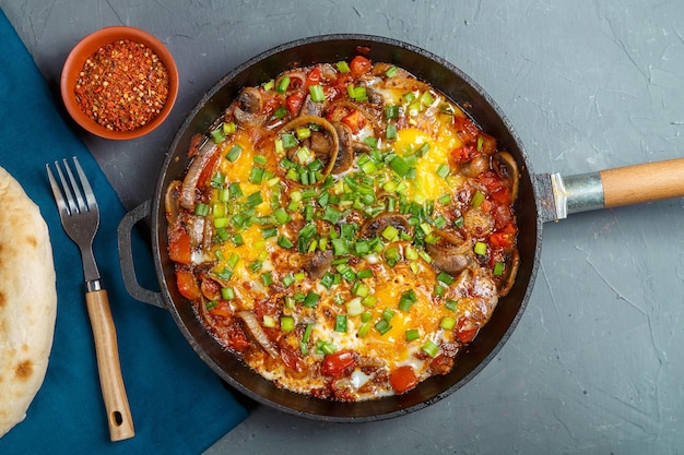 Shakshuka in a frying pan on a gray background next to a fork and spices on a blue napkin Horizontal