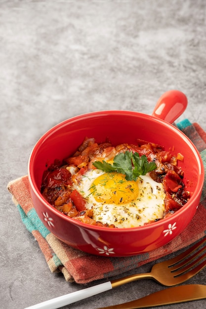 Shakshuka in een rode pan, grijze achtergrond, kopie ruimte