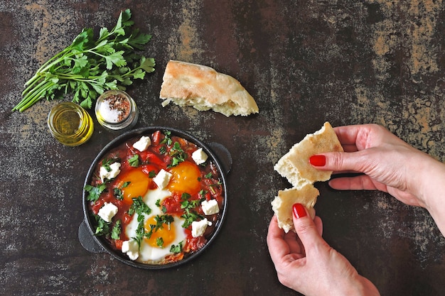 Shakshuka with pita bread. Middle Eastern cuisine. Arabic, Israeli, Moroccan breakfast or lunch. Fried eggs in tomato and vegetable sauce with spices and herbs.