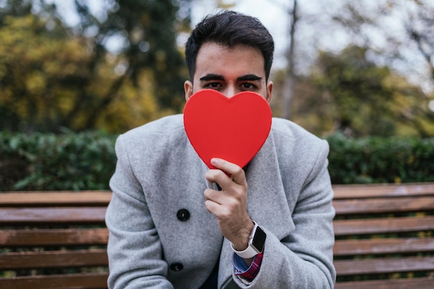 口を覆う赤いハートを持つ男性の浅い焦点のクローズアップ – コンセプトバレンタインデー