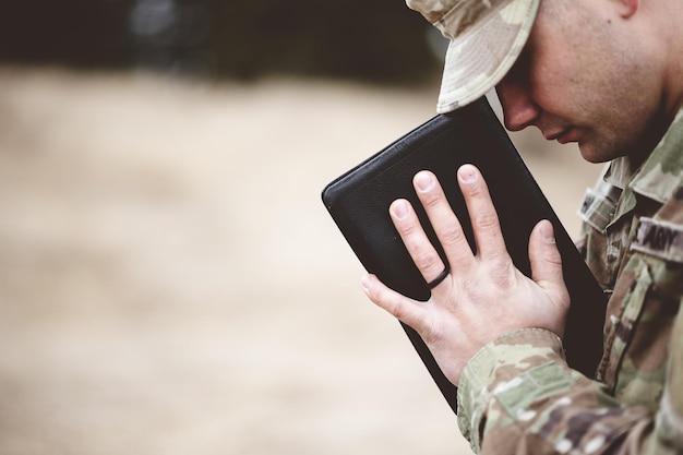 Shallow focus shot of a young soldier praying while holding the bible