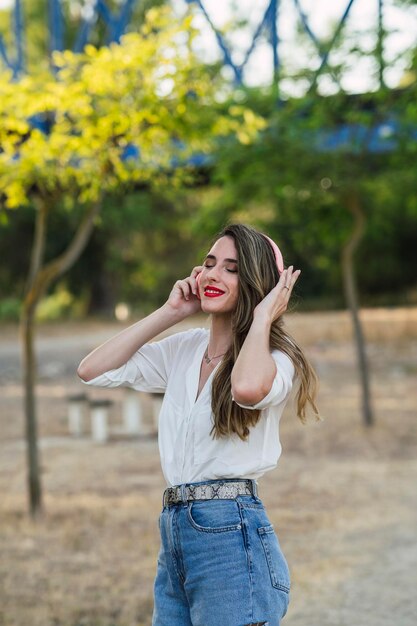 Shallow focus of a young cheerful Spanish woman listening to music with headphones in a park