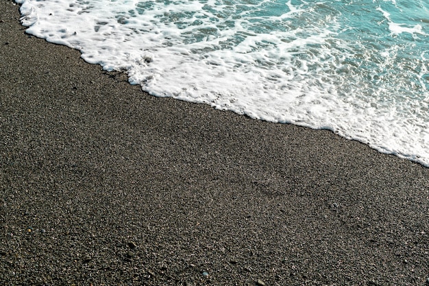 Shallow volcanic black sandy beach, blue water waves and wet dark sand on the sea coast.