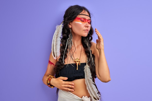 Shamanic female with Indian feather on hair and colourful painted make-up, portrait in studio. indian ethnicity