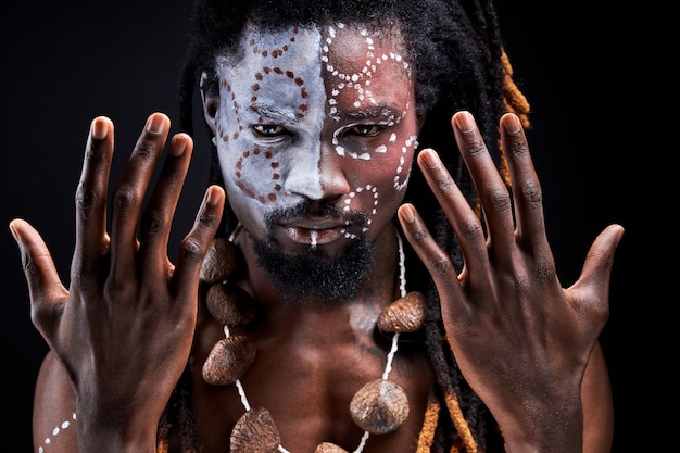 Shamanic man stand doing rituals, spreading hands, portrait of\
black guy with ethnic make-up isolated