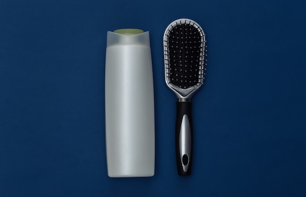 Photo shampoo bottle and hair brush on classic blue background. color 2020. top view