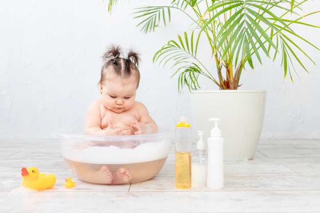 Shampoo bottles in focus against the a baby washing in a basin with foam