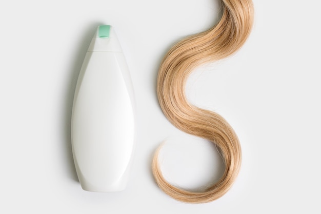 Bottiglia di shampoo o balsamo e ciocca di capelli biondi ricci isolati su sfondo chiaro, vista dall'alto. disposizione piatta, copia spazio per il testo. cosmetici per la cura dei capelli, prodotti di bellezza per la cura dei capelli, trattamento dei capelli.