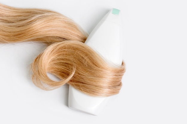 Photo shampoo or conditioner bottle wrapped in lock of curly blonde hair isolated on light background, top view. flat lay, copy space for text. hair care cosmetics, beauty haircare products, hair treatment.