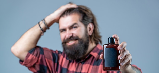 Shampoo conditioner for men. Expert care for demanding hair. Plastic container with shampoo. Young handsome man applying cream lotion. Man holds black bottle of shampoo or shower gel.