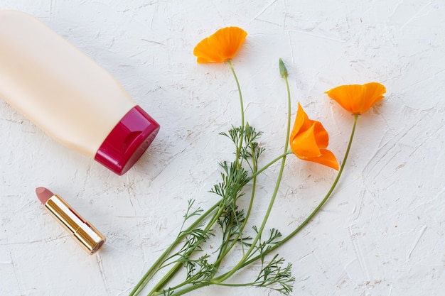 Shampoo, een lipstick en oranje bloemen op een witte ondergrond