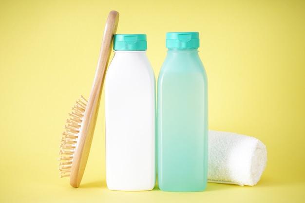 Shampoo, fles conditioner en houten haarborstel op gele achtergrond.