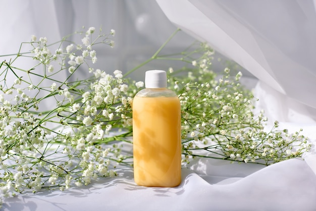 Shampoo, gel or lotion on transparent plastic bottle with lid on white background with spring flowers