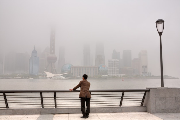 上海、中国大気汚染、重いスモッグに包まれた高層ビル、市の空気はひどく汚染されたままで、外灘に立っている人が浦東地区を見ています。