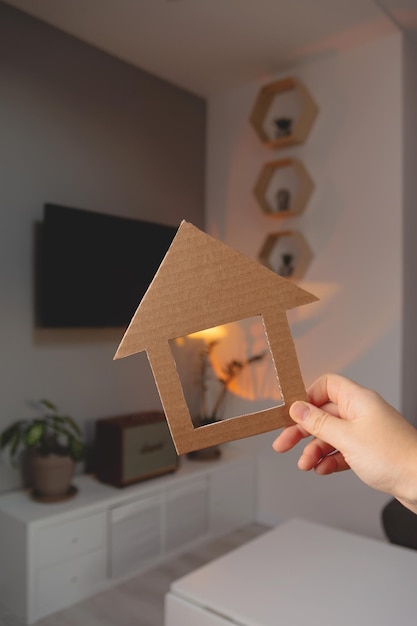 Форма дома в руке женщины на фоне минималистичного интерьера