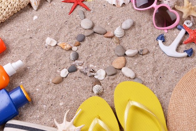 Форма солнца из морских раковин и камней на песке с пляжными аксессуарами