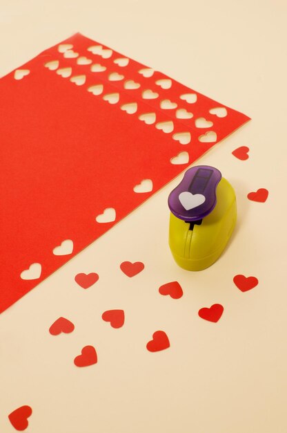 Shaped hole punch and hearts made of red colored paper on a beige background in vertical format