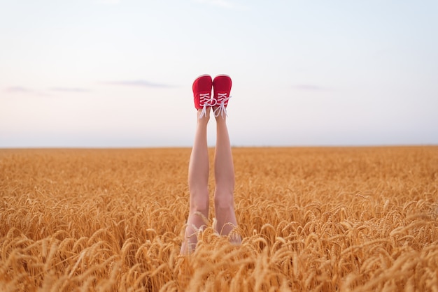 Shapely female legs stick out of wheat field. Vegetarian concept.