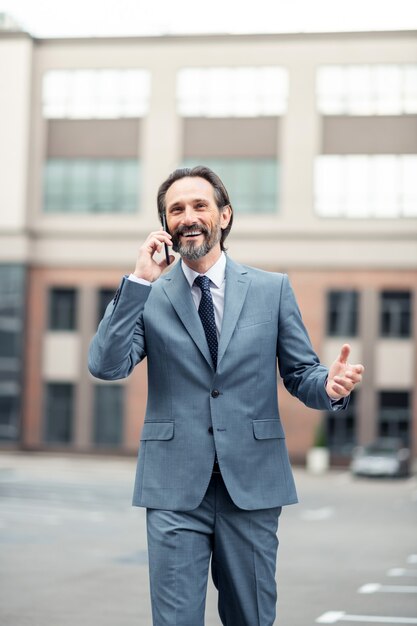 Sharing good news. Cheerful handsome grey-haired businessman calling wife while sharing good news