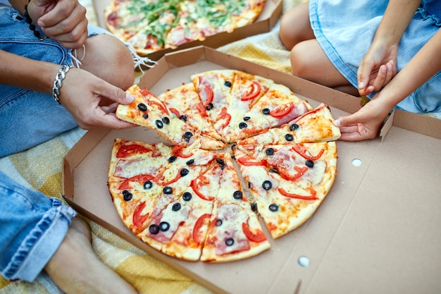 Sharing pizza, hands taking a piece of pizza from a box outdoor,