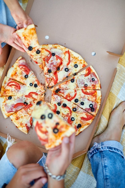 Sharing pizza, hands taking a piece of pizza from a box outdoor,