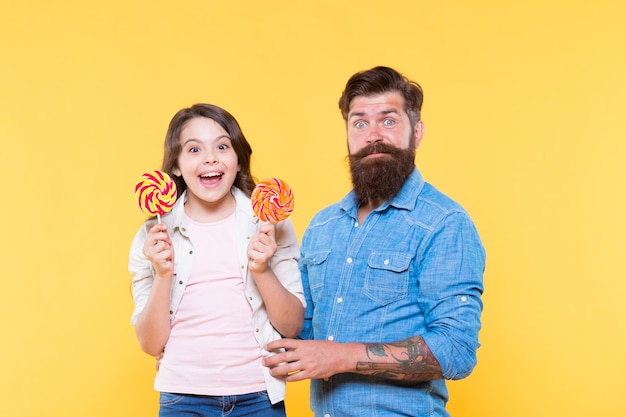 Sharing sweets with dearest people Daughter and father eat sweet candies Sweet childhood Girl child and dad hold colorful lollipops Sweet dessert Bearded hipster good daddy for adorable daughter