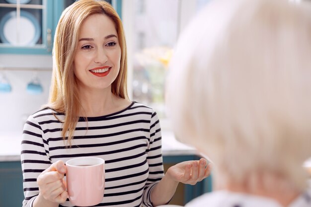 写真 考えを共有する。かなり若い女性が年配の母親と話し、彼女の一日について話し、コーヒーを飲みながら彼女に愛情を込めて微笑むことに焦点を当てています