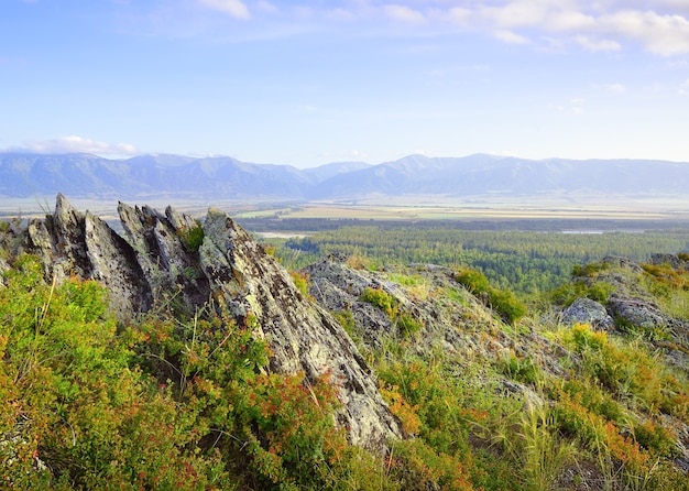 Sharp rocks on the top of a mountain above a mountain valley under a blue cloudy sky Siberia