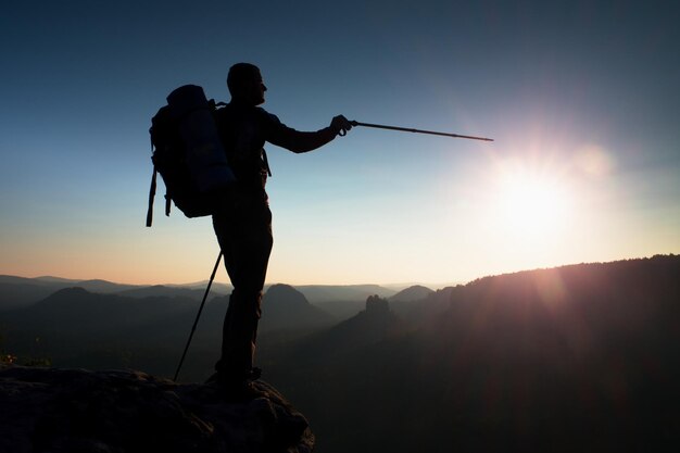 フレームの太陽とともに山の頂上にある背の高い男のいシルエット