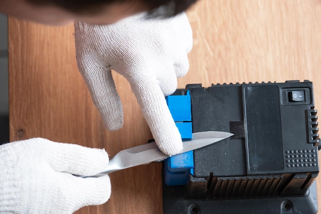 Sharpening a knife on an electric sharpener at home The man's hand drives the knife blade between the blue sharpeners dust flies on the machine