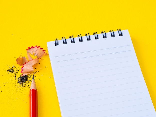 Sharpening a red pencil sharpener and the note book on yellow background.