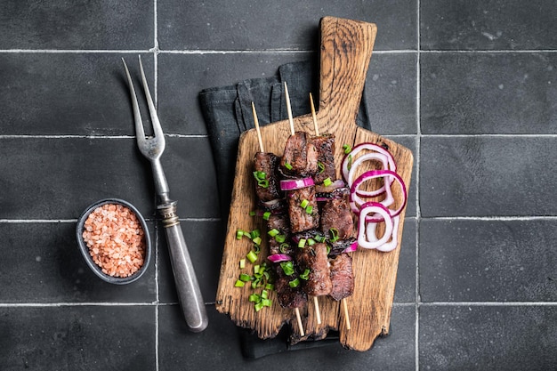 Shashlik grilled meat skewers shish kebab with beef and lamb meat onion and herbs Black background Top view