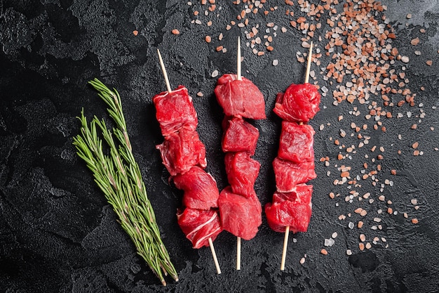 Shashlik rauw rundvlees kalfsvlees shish kebab, vlees met kruiden op spiesjes. Zwarte achtergrond. Bovenaanzicht.