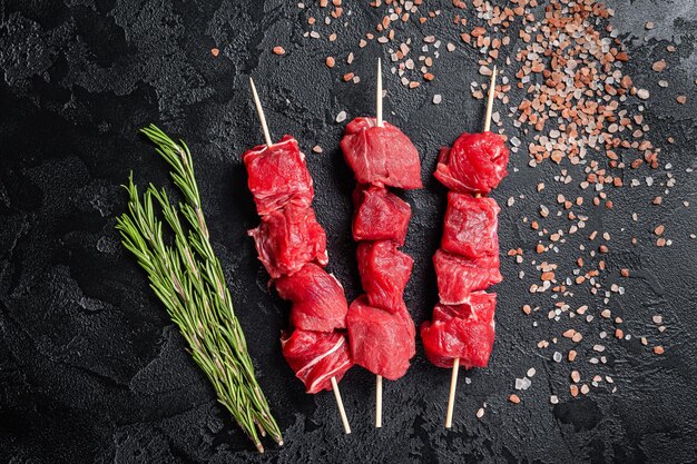 Shashlik raw beef veal shish kebab, Meat with herbs on Skewers. Black background. Top view.