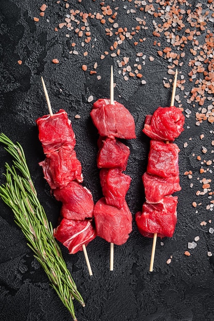 Shashlik raw beef veal shish kebab Meat with herbs on Skewers Black background Top view