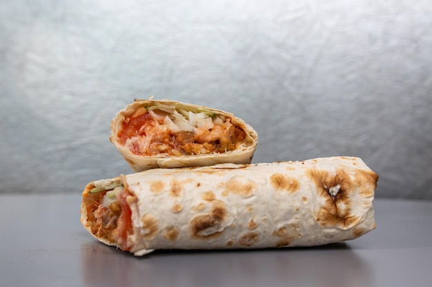 shaurma in pita bread with chicken and vegetable filling on a gray background